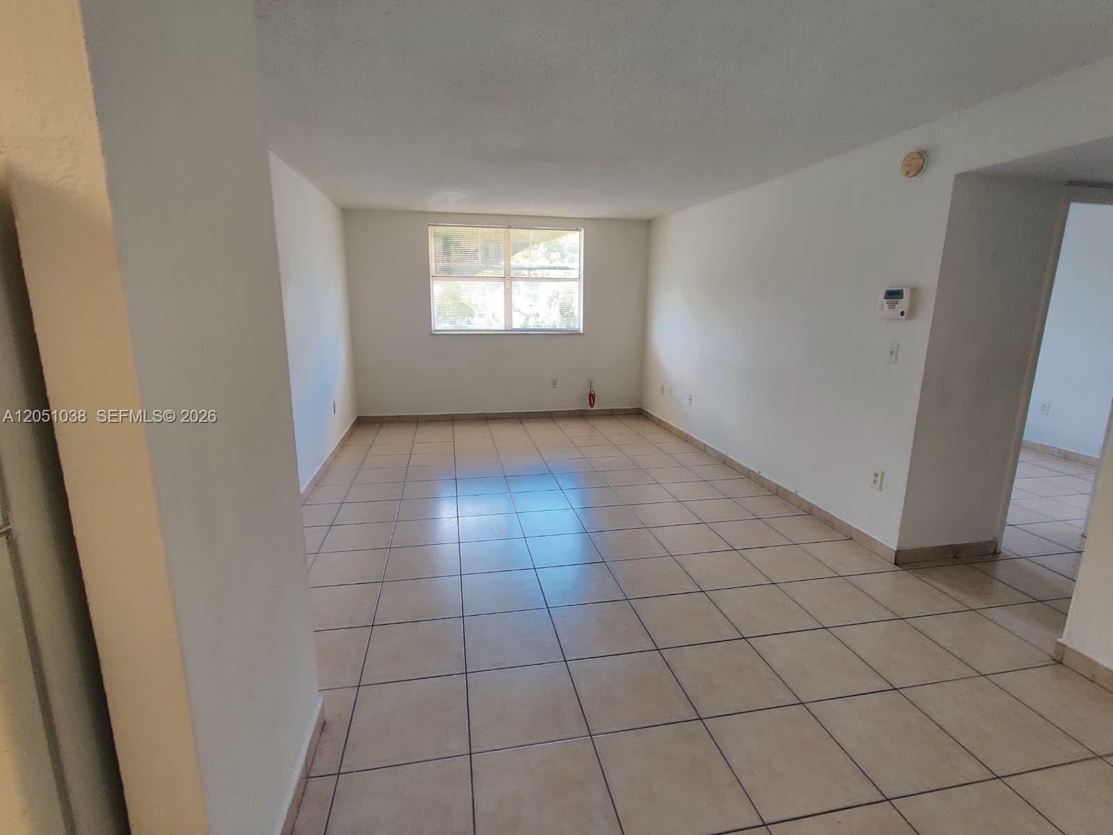 An empty room features white walls, tan tile flooring, and a single window — 666 W 81st St # 414, Hialeah FL 33014, HIALEAH, FL