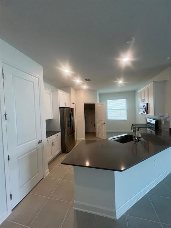 A kitchen features white cabinets, dark countertops, stainless steel appliances, and light-colored tile flooring — 2557 PEACE OF MIND AVENUE, KISSIMMEE, FL