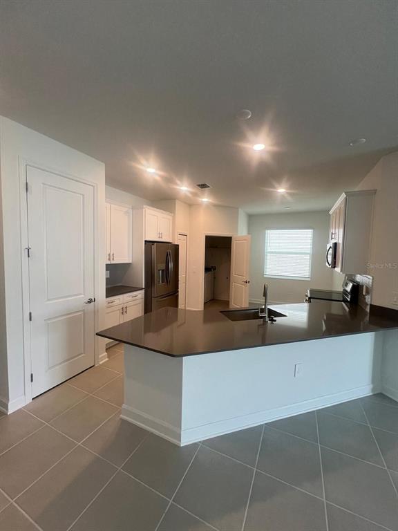 A kitchen features white cabinetry, dark countertops, a breakfast bar, and light-colored tile flooring — 2557 PEACE OF MIND AVENUE, KISSIMMEE, FL
