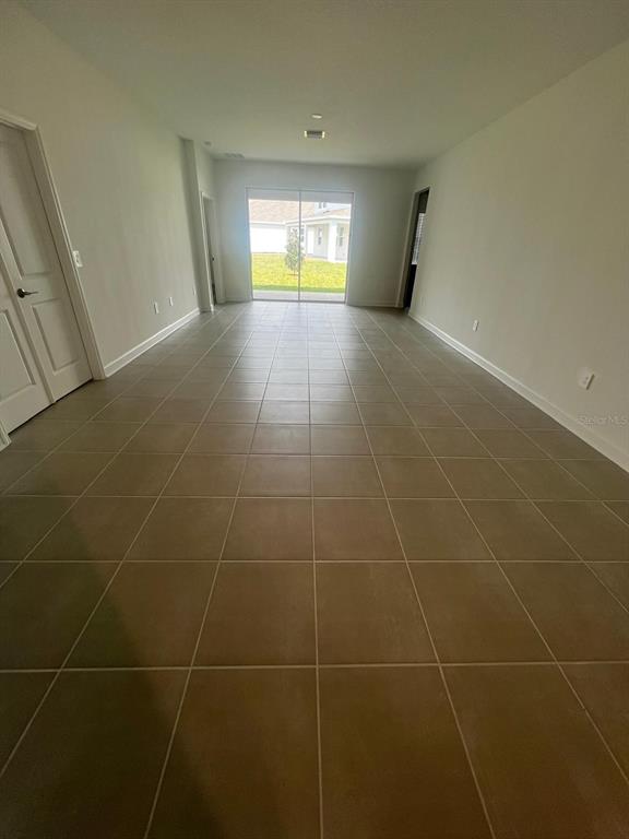An empty room with light-colored walls and large square floor tiles leads to sliding doors — 2557 PEACE OF MIND AVENUE, KISSIMMEE, FL