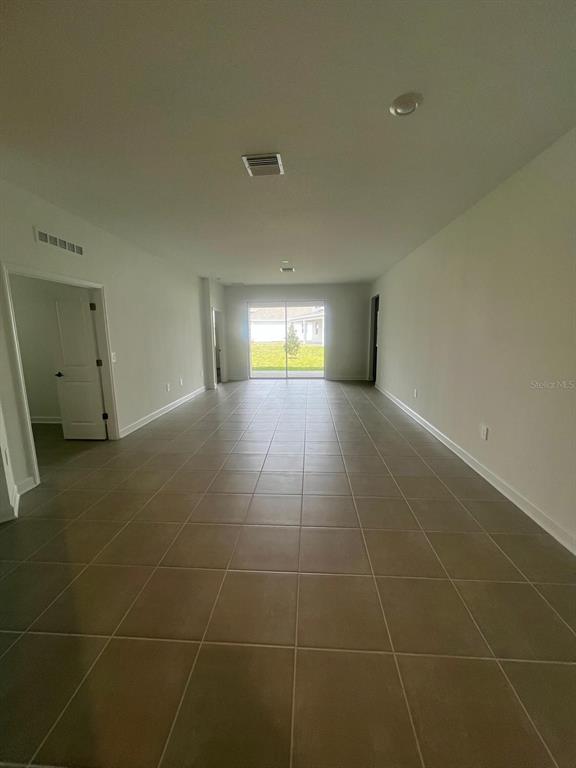 An open-concept living area features light-colored walls, large floor tiles, and sliding glass doors — 2557 PEACE OF MIND AVENUE, KISSIMMEE, FL