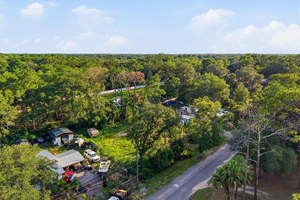 An aerial view shows a rural property with a house, outbuildings, and vehicles among trees — 88 W SIMON AVENUE, APOPKA, FL