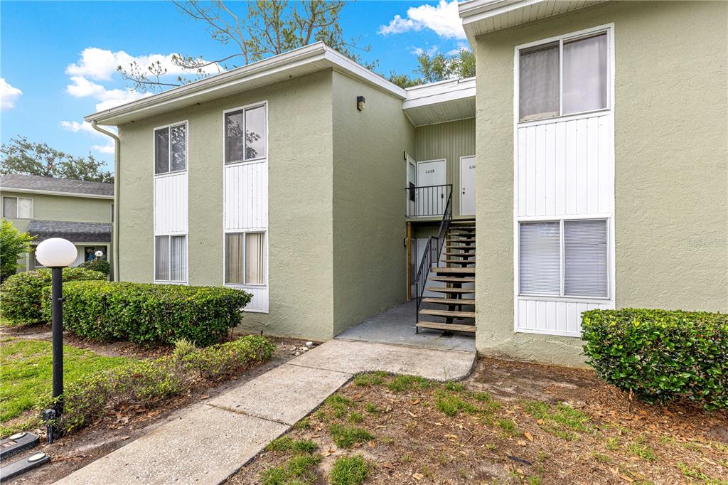 An exterior view of a two-story apartment building with green stucco walls and stairs — 608 FAIRWAYS CIRCLE UNIT B, OCALA, FL