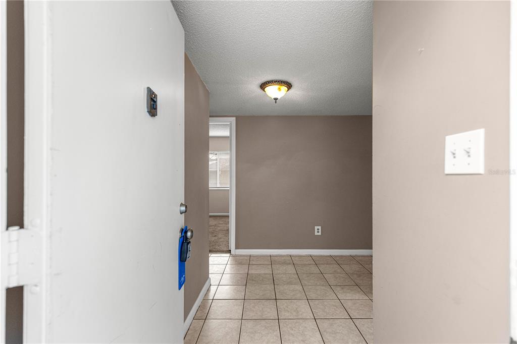 An entryway with tan tile flooring leads to a carpeted room through a doorway — 608 FAIRWAYS CIRCLE UNIT B, OCALA, FL