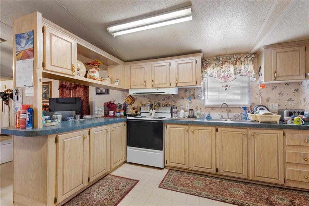 A kitchen features light wood cabinets, blue laminate countertops, a white stove, and floral wallpaper — 187 SE LOXLEY GLEN, LAKE CITY, FL