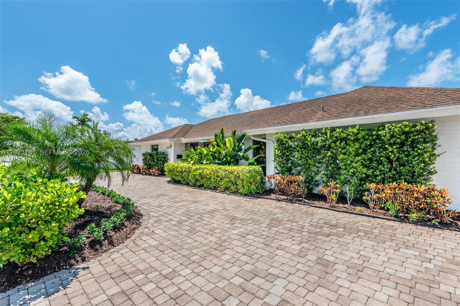 A paved driveway leads to a white house with a brown roof and landscaped hedges — 2330 NE 195th St, Miami FL 33180, MIAMI, FL