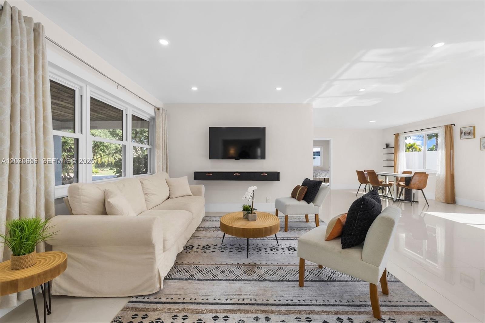 A bright living room features a beige sofa, two accent chairs, and a wall-mounted television — 416 NE 29th St, Wilton Manors FL 33334, WILTON MANORS, FL