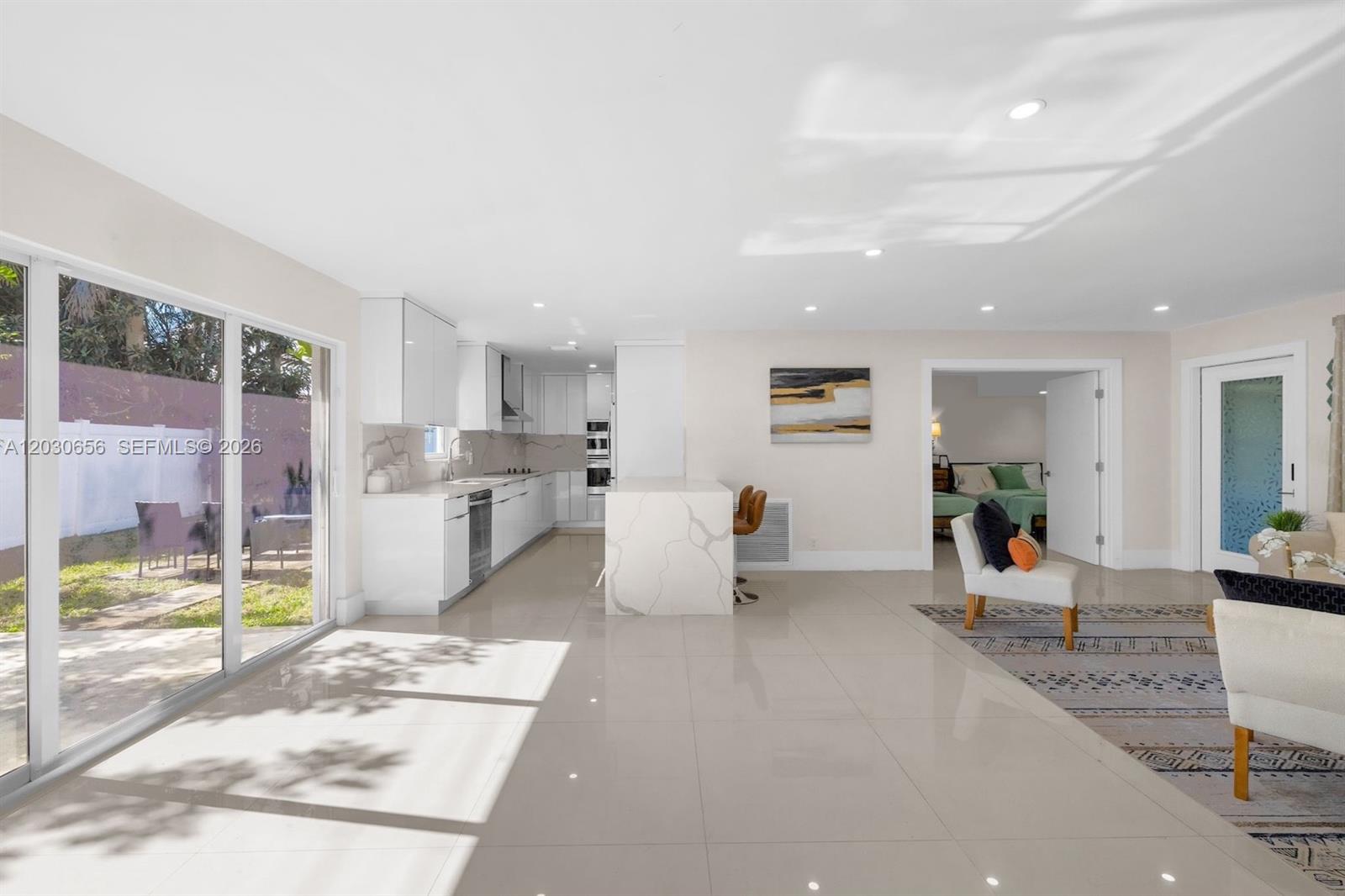 A modern open-concept kitchen and living area features white cabinetry, marble-topped island, and tile flooring — 416 NE 29th St, Wilton Manors FL 33334, WILTON MANORS, FL