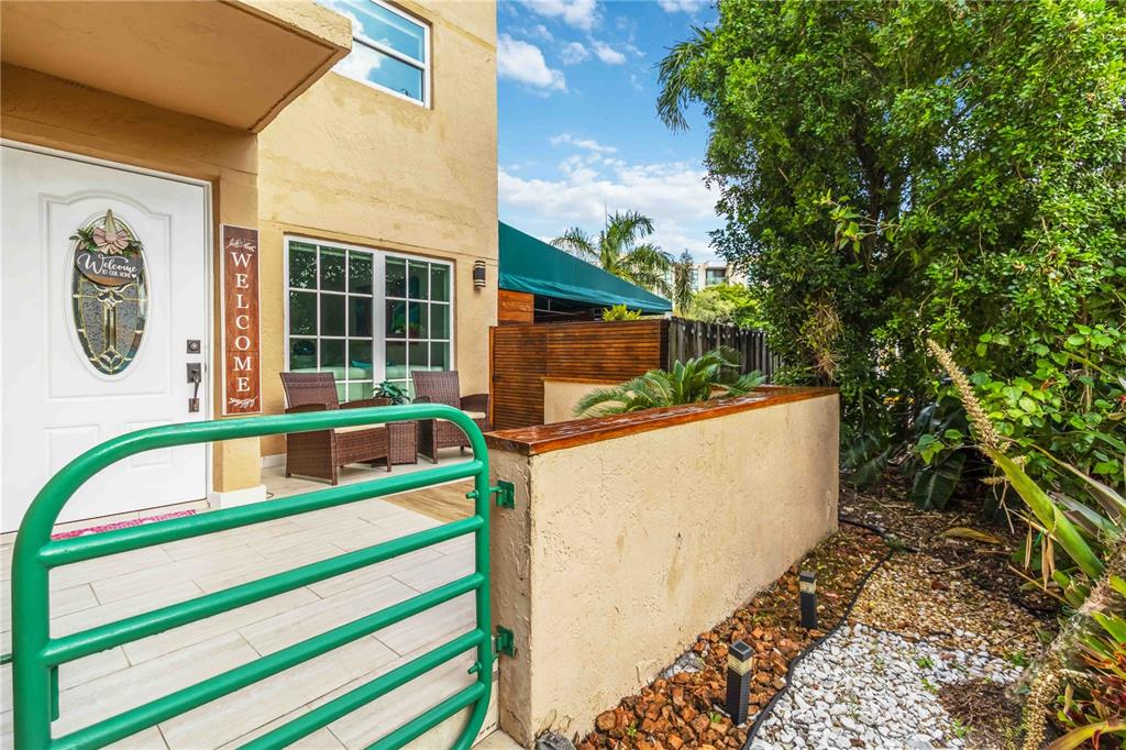 A green metal gate opens to a patio with wicker chairs and a tan wall — 11880 SW 19TH LANE UNIT 165, MIAMI, FL