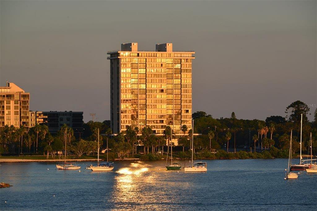 A tall residential building stands on a waterfront with several sailboats moored in the foreground — 770 S PALM AVENUE UNIT 904, SARASOTA, FL