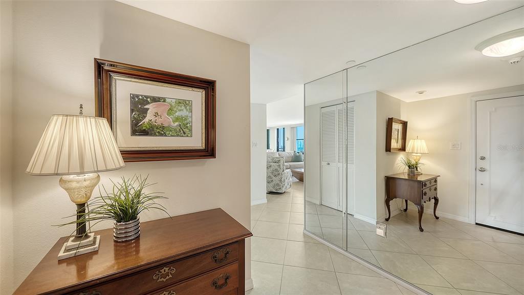 An entryway features a wooden dresser, a lamp, a framed print, and mirrored closet doors — 770 S PALM AVENUE UNIT 904, SARASOTA, FL