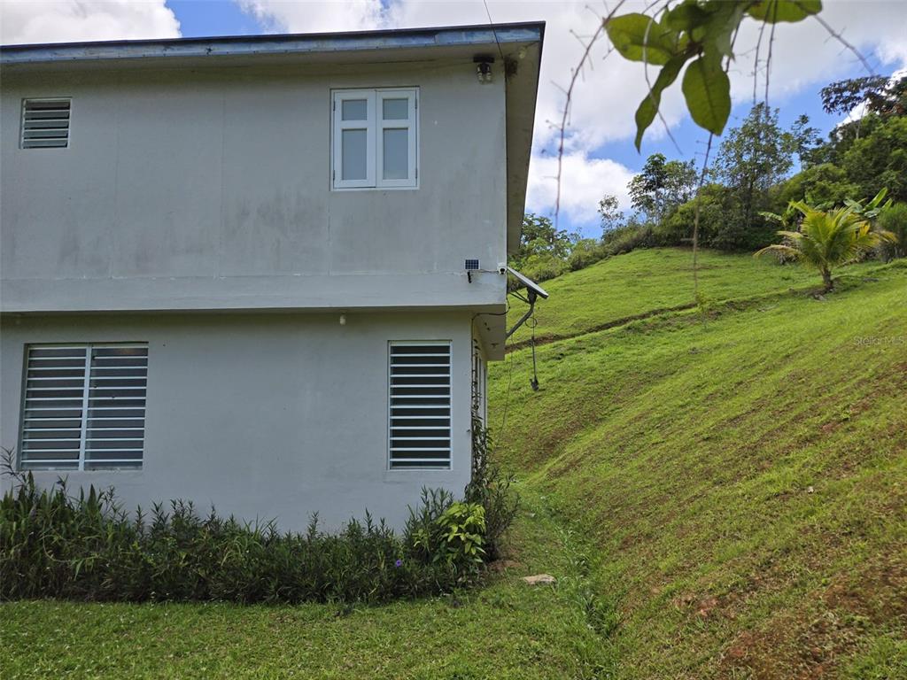 A two-story house exterior with a grassy hillside and a small solar panel — Carr 813 KM 2.5 INT, NARANJITO, PR