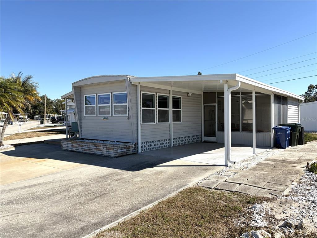 A light gray manufactured home features a concrete driveway, a carport, and a screened porch — 1862 PALM SPRINGS STREET, SARASOTA, FL
