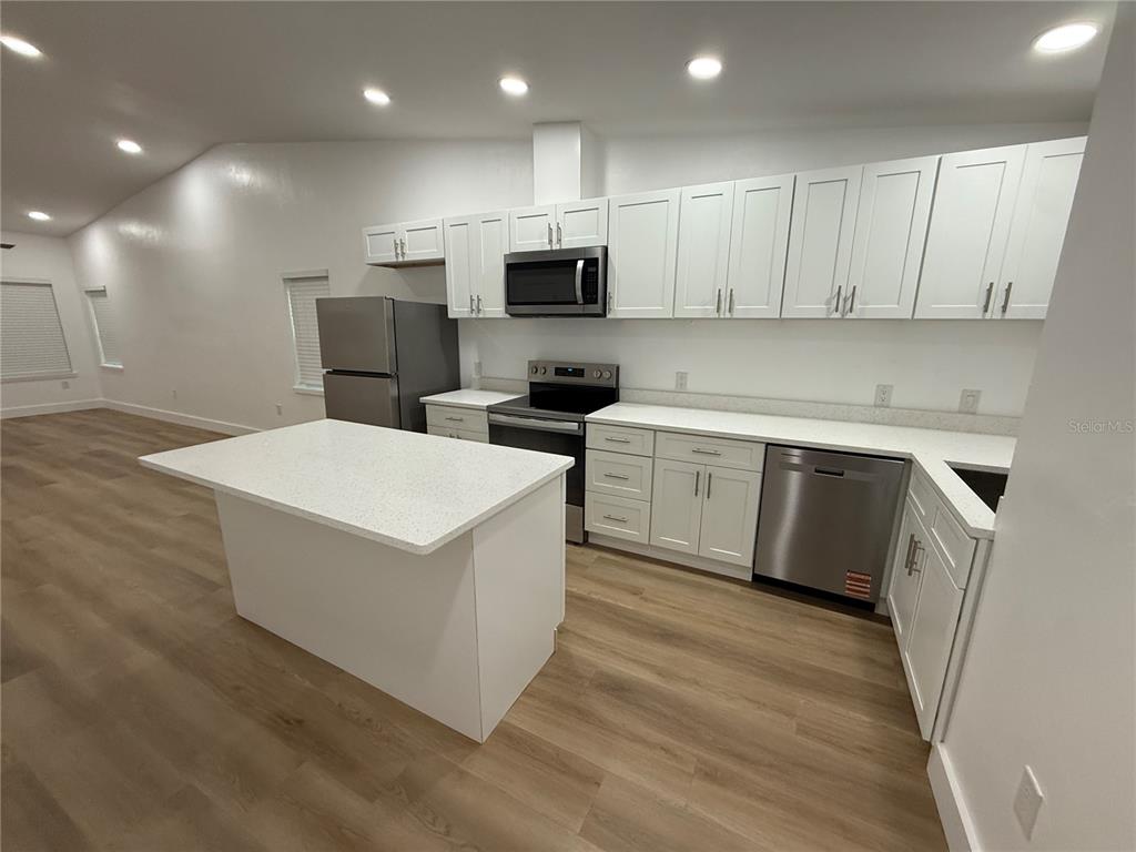 A kitchen features white cabinets, stainless steel appliances, a center island, and light wood flooring — 7020 SW 45TH AVENUE, GAINESVILLE, FL