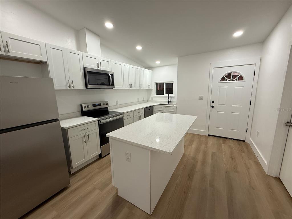 A kitchen features white cabinets, stainless steel appliances, a center island, and light wood flooring — 7020 SW 45TH AVENUE, GAINESVILLE, FL