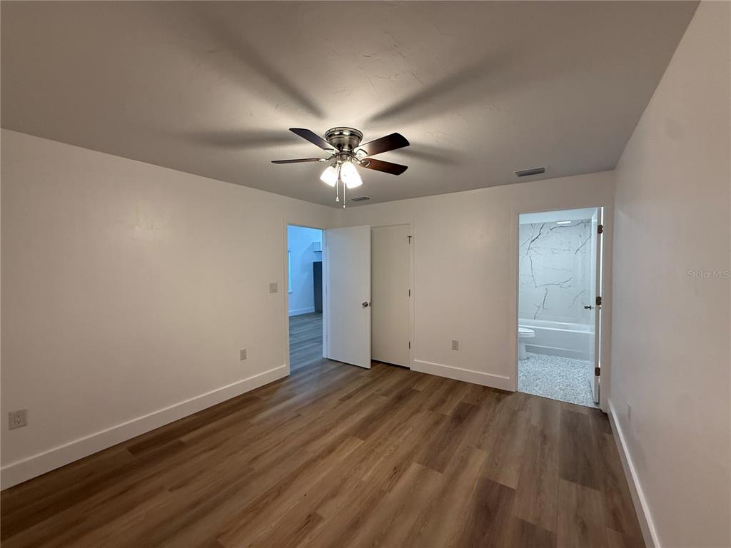 A bedroom with wood-look flooring, a ceiling fan, and an attached bathroom — 7020 SW 45TH AVENUE, GAINESVILLE, FL