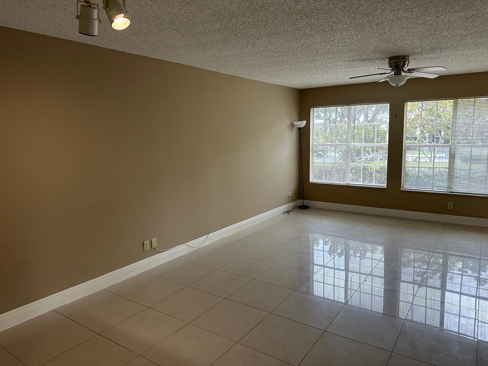 An empty room features tan walls, large windows with blinds, and glossy tiled flooring — 6283 La Costa Drive # D, Boca Raton FL 33433, BOCA RATON, FL