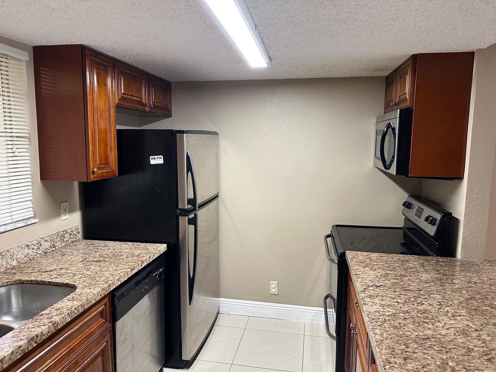 A kitchen features wood cabinets, granite countertops, stainless steel appliances, and tile flooring — 6283 La Costa Drive # D, Boca Raton FL 33433, BOCA RATON, FL