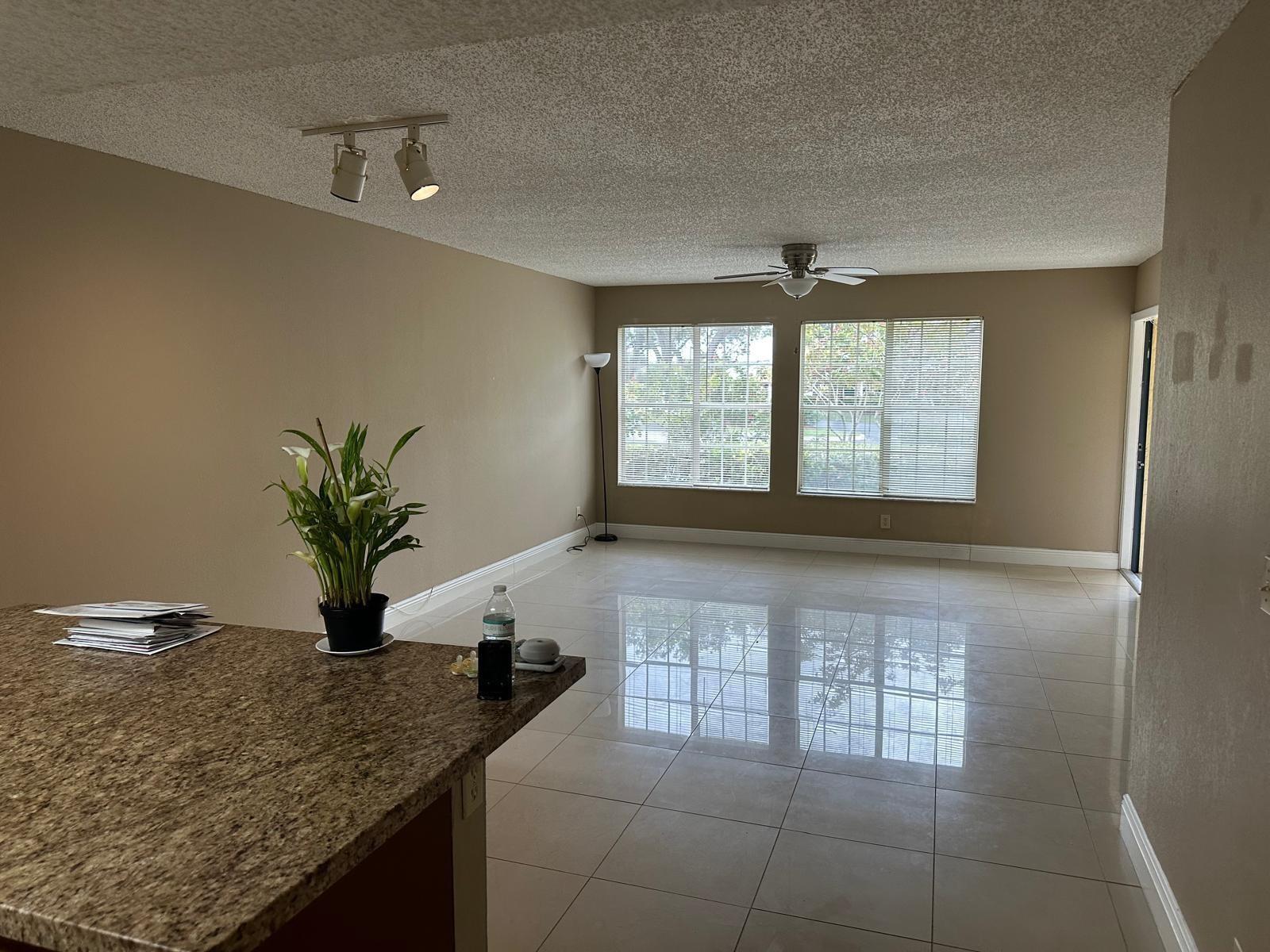 An open living area features beige walls, tile flooring, a ceiling fan, and two windows — 6283 La Costa Drive # D, Boca Raton FL 33433, BOCA RATON, FL