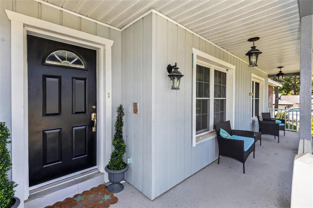 A covered front porch features a black door, light gray siding, and outdoor seating — 2031 TOURNAMENT DRIVE, APOPKA, FL