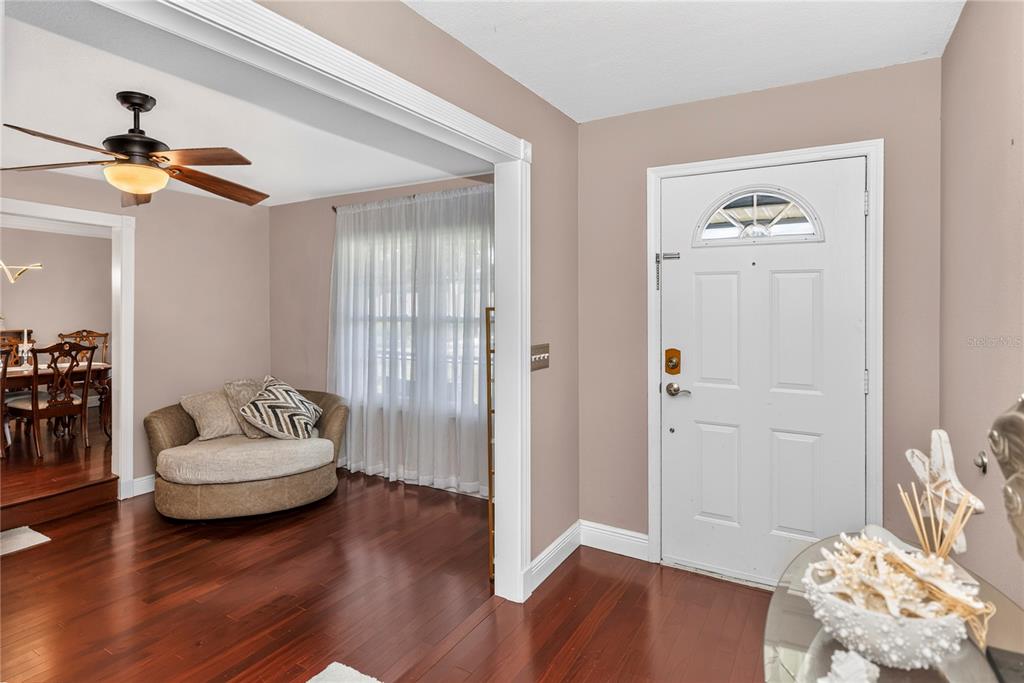 An entryway with hardwood floors, a white front door, and a view into a dining room — 2031 TOURNAMENT DRIVE, APOPKA, FL