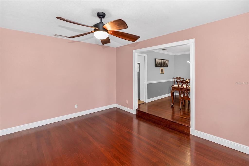 A room with pink walls and dark hardwood floors leads to a raised dining area — 2031 TOURNAMENT DRIVE, APOPKA, FL