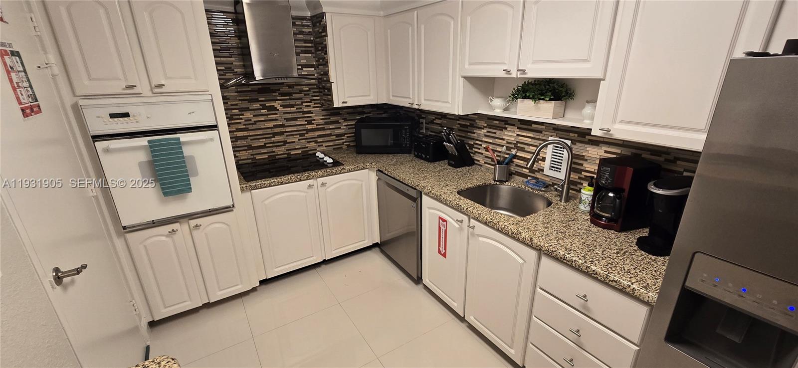 A kitchen features white cabinets, a granite countertop, a stainless steel sink, and a backsplash — 4001 S Ocean Dr # 4J, Hollywood FL 33019, HOLLYWOOD, FL