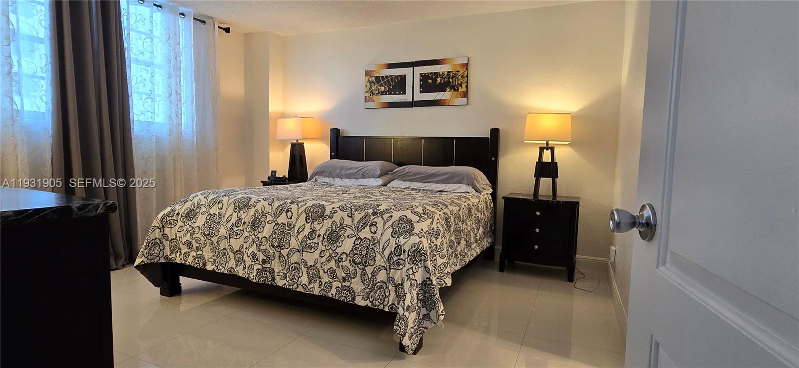 A bedroom features a black bed frame, patterned bedding, two nightstands with lamps, and tile floors — 4001 S Ocean Dr # 4J, Hollywood FL 33019, HOLLYWOOD, FL