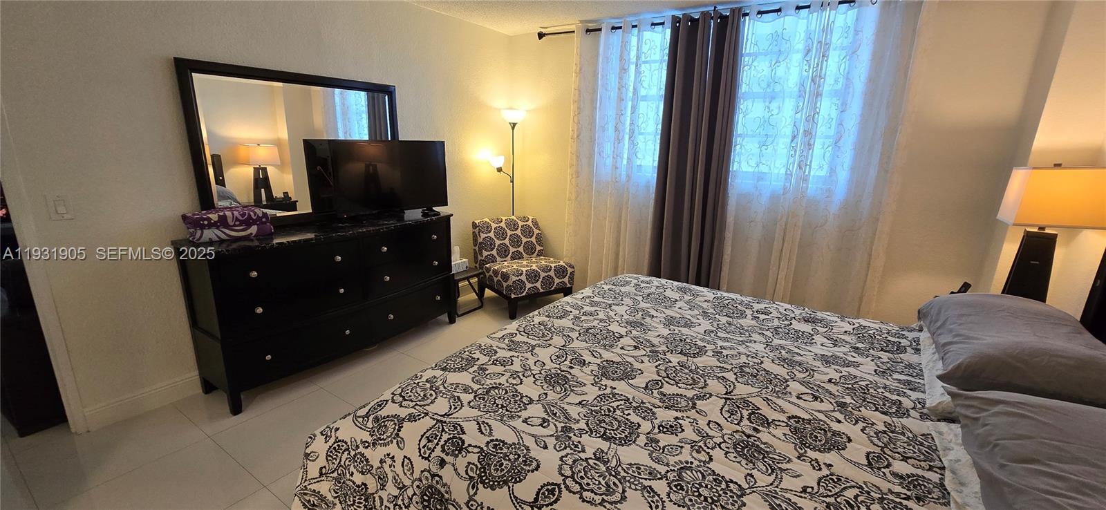 A bedroom features a bed with a patterned comforter, a black dresser, and a window — 4001 S Ocean Dr # 4J, Hollywood FL 33019, HOLLYWOOD, FL