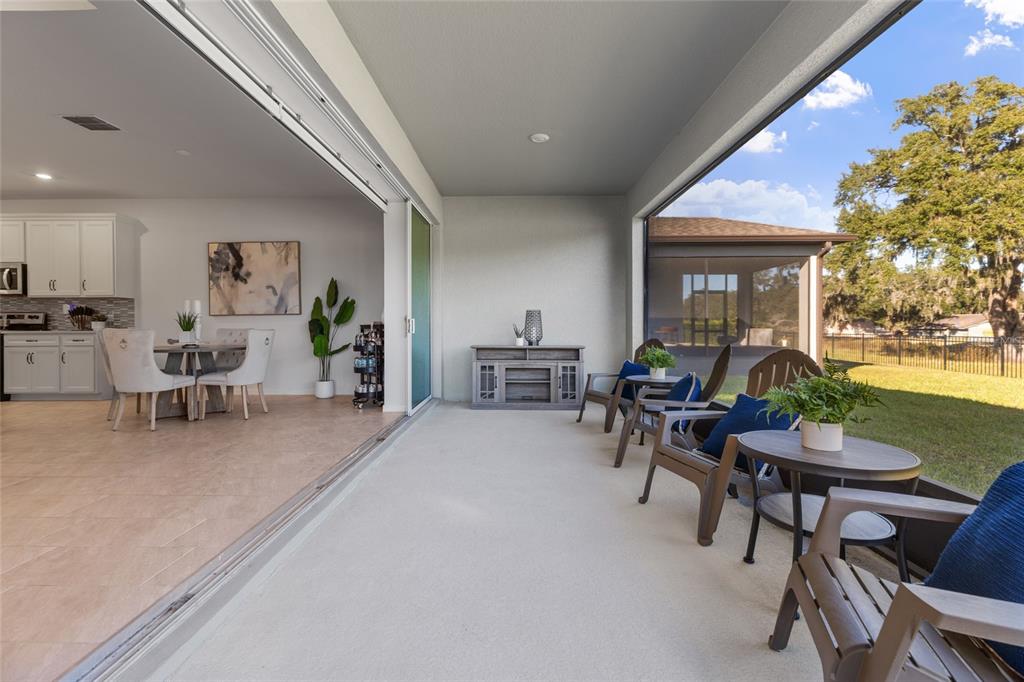 A covered patio with outdoor seating overlooks a backyard through a large sliding glass door — 6248 BRADFORD WOODS DR, ZEPHYRHILLS, FL