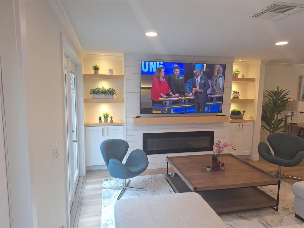 A living room features a fireplace, wall-mounted television, built-in shelving, and two blue accent chairs — 1203 LYRIC LANE, SARASOTA, FL