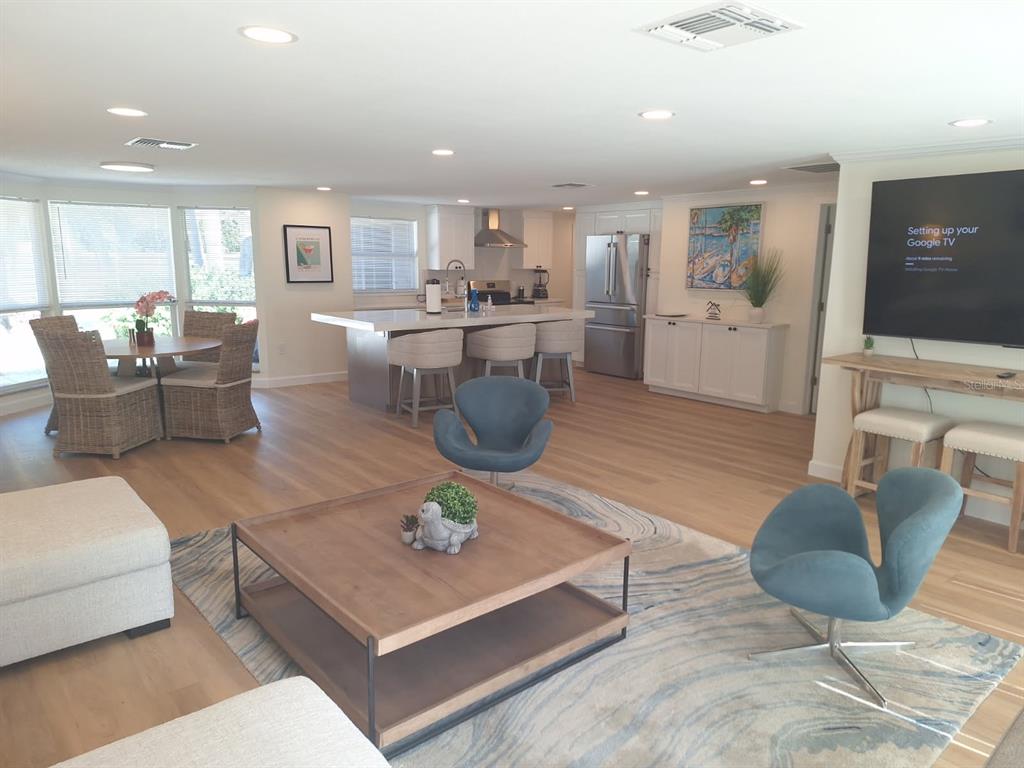 An open-concept living room and kitchen featuring light wood floors, a central island, and furniture — 1203 LYRIC LANE, SARASOTA, FL