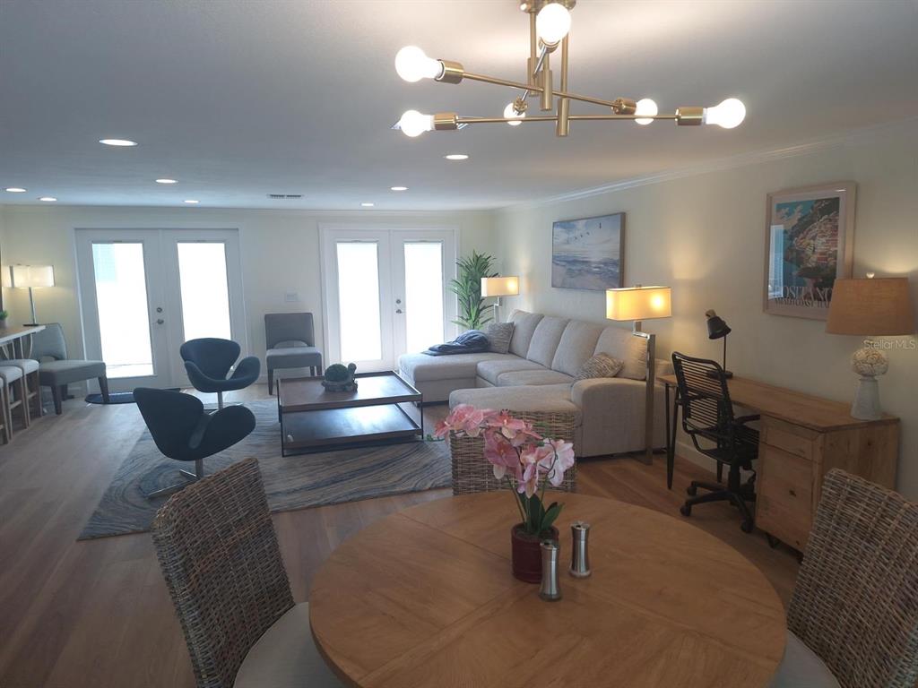 An open-concept living and dining area features a sectional sofa, modern chandelier, and wood flooring — 1203 LYRIC LANE, SARASOTA, FL