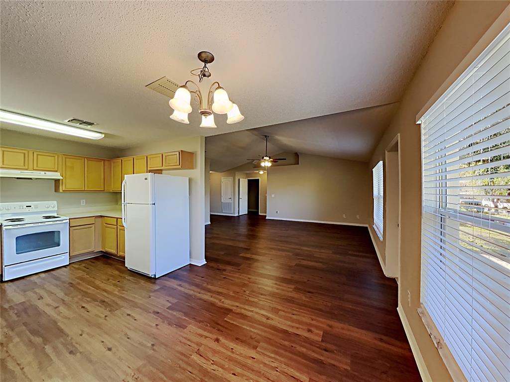 A kitchen with light wood cabinets and white appliances opens into a spacious living area — 1745 PILCHARD DRIVE, POINCIANA, FL