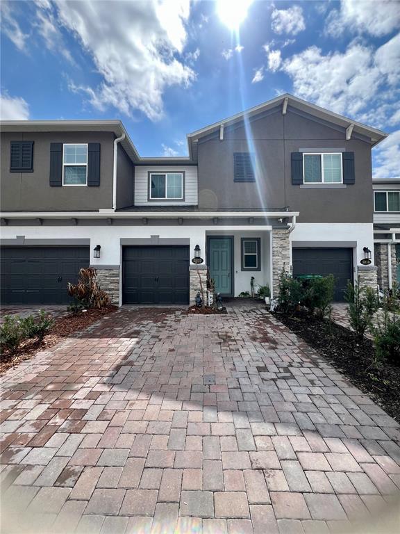 A two-story townhouse exterior features a paver driveway, dark garage doors, and stone accents — 5222 TYSON RANCH BOULEVARD, ORLANDO, FL