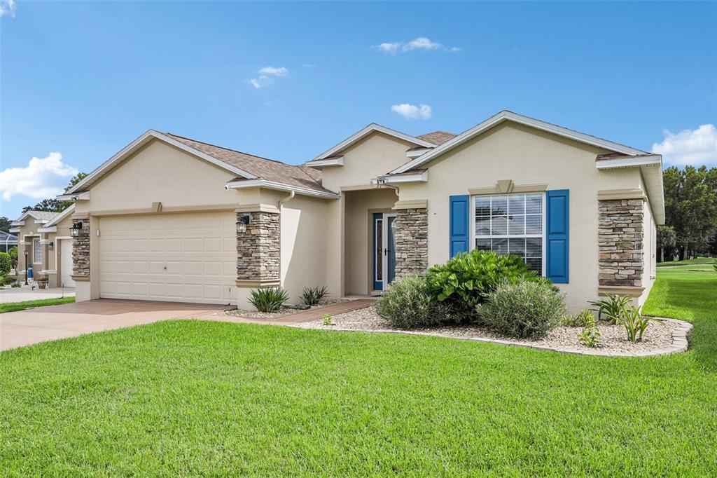 A single-story suburban house with a tan stucco exterior, stone accents, and a two-car garage — 1056 SW 159TH STREET, OCALA, FL