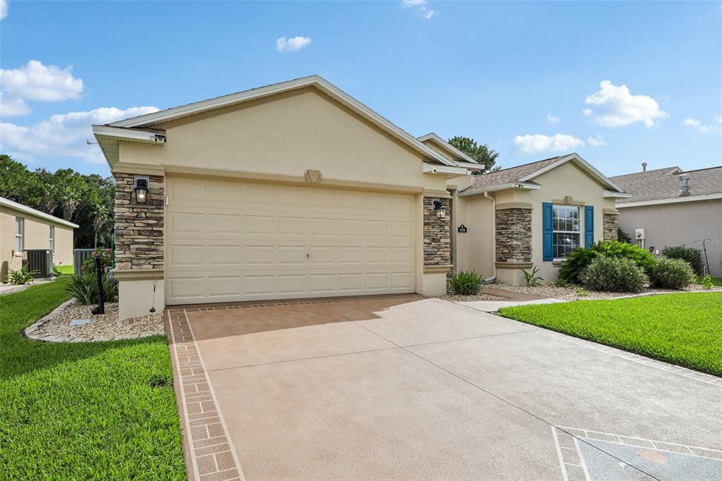 A beige suburban house features a two-car garage, stone accents, and a concrete driveway — 1056 SW 159TH STREET, OCALA, FL