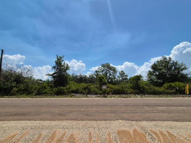 A vacant, overgrown lot sits behind a paved road under a blue sky — 3040 W HASBROUCK ROAD, AVON PARK, FL