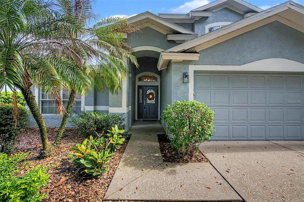 A single-story house exterior features a gray stucco facade, a front walkway, and a palm tree — 5418 TWIN CREEKS DRIVE, VALRICO, FL