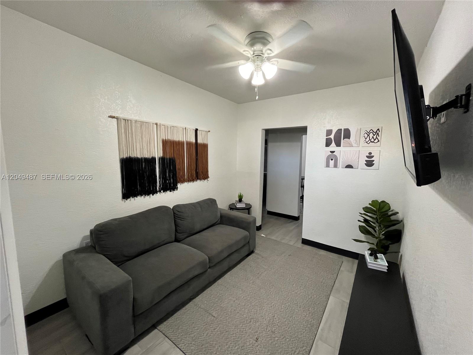 A living room features a gray sofa, a wall-mounted television, and a ceiling fan — 140 NW 13th St, Miami FL 33136, MIAMI, FL