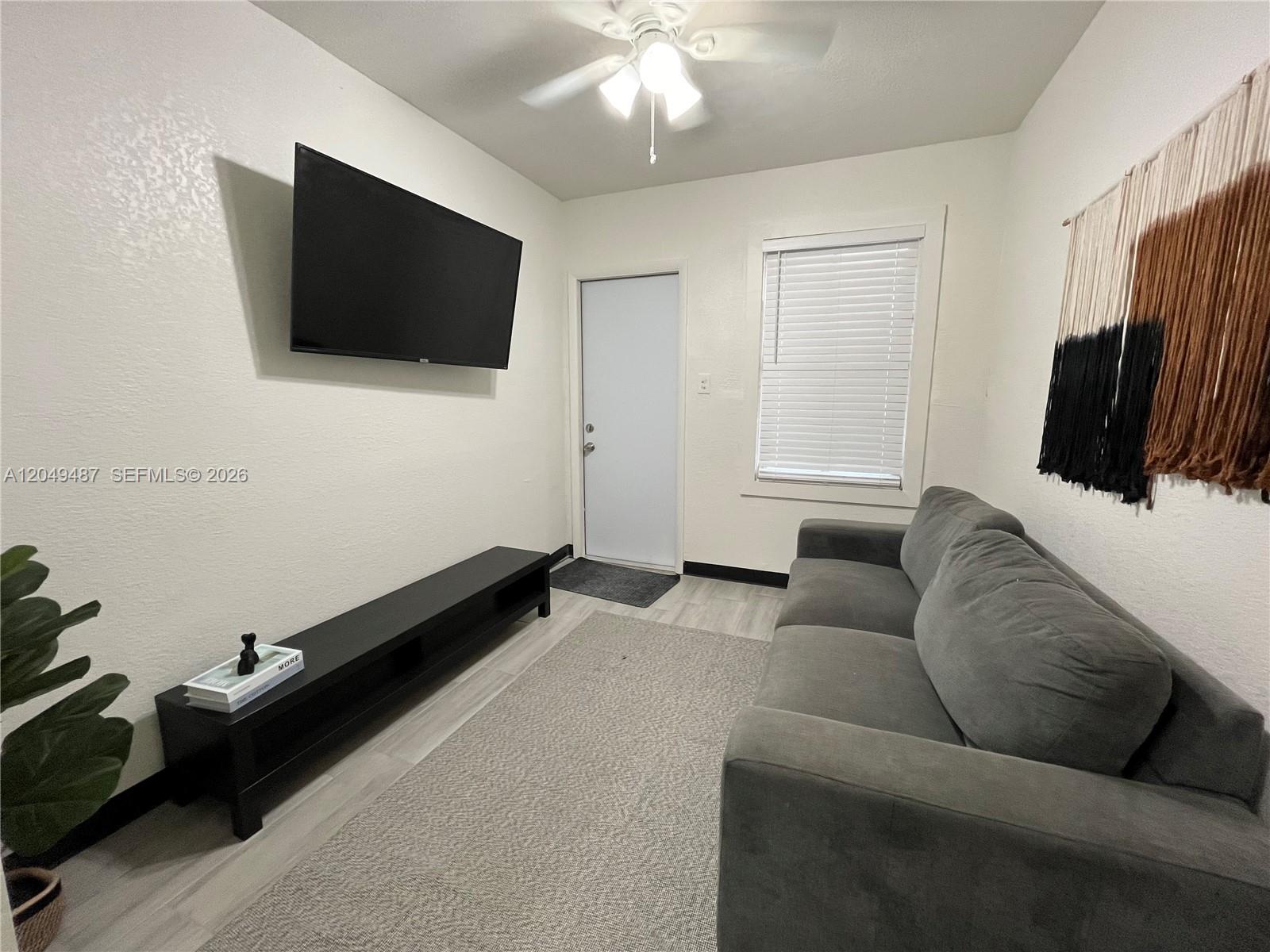A living room features a wall-mounted television, a grey sofa, and a black media console — 140 NW 13th St, Miami FL 33136, MIAMI, FL