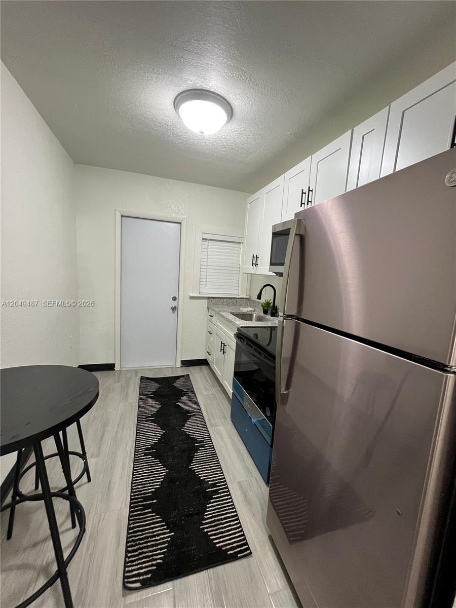 This kitchen features white cabinets, stainless steel appliances, a black runner rug, and light flooring — 140 NW 13th St, Miami FL 33136, MIAMI, FL