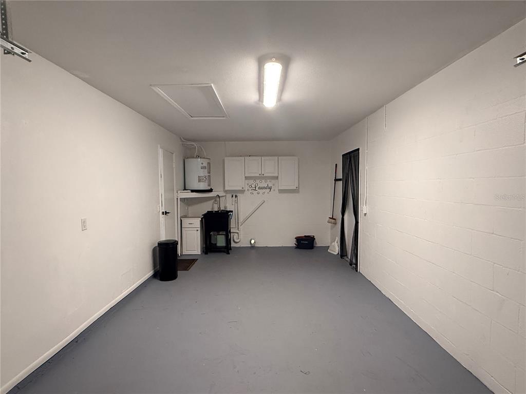 A garage with a painted gray floor, a utility sink, and white wall-mounted cabinets — 13186 THRUSH STREET, SPRING HILL, FL