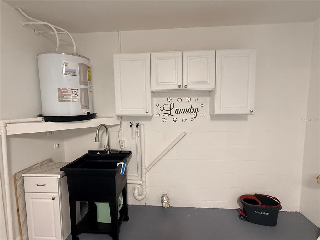 A laundry room features a utility sink, a water heater, and white wall-mounted cabinets — 13186 THRUSH STREET, SPRING HILL, FL