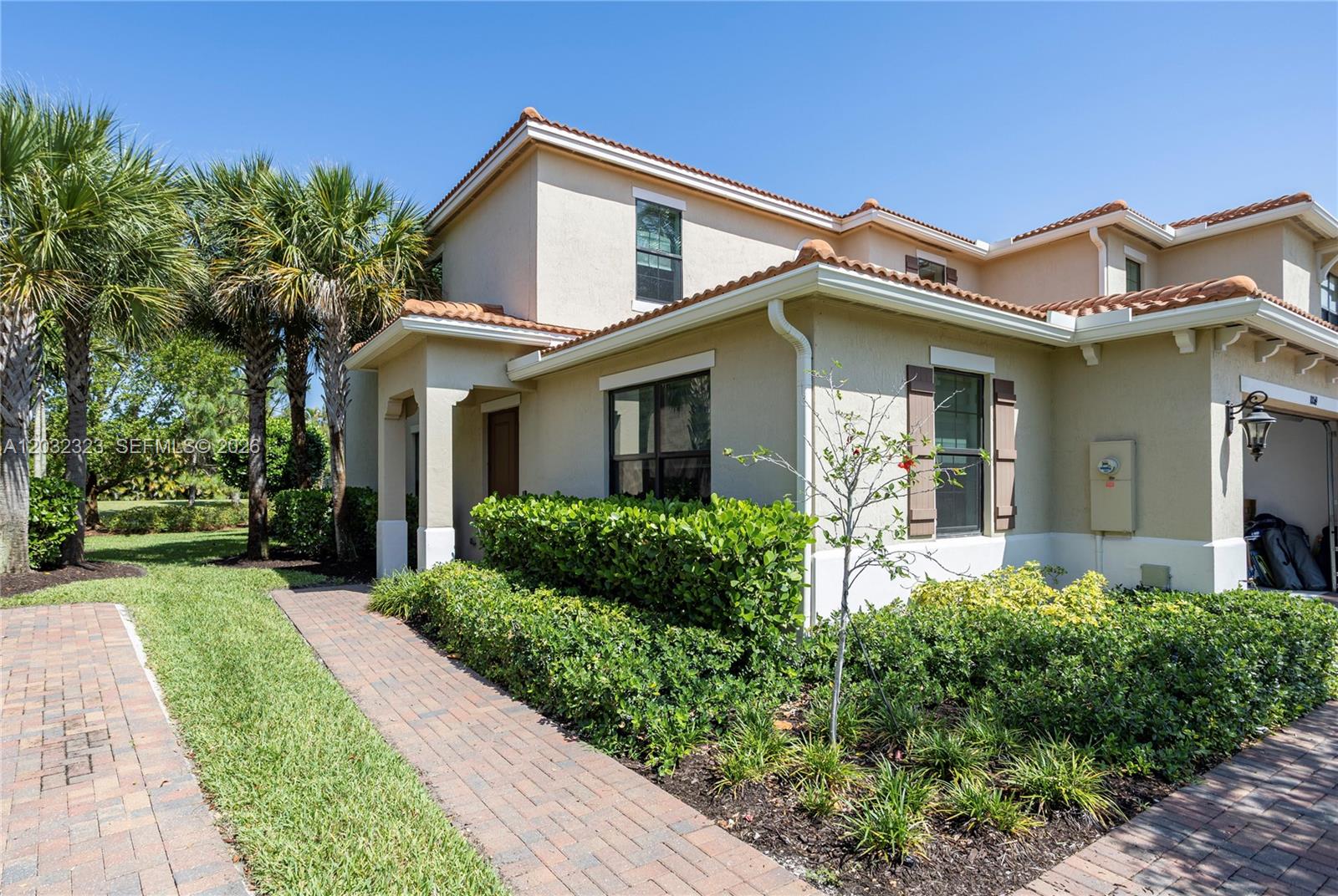 A two-story tan stucco townhouse features a tiled roof, brick walkway, and landscaped front yard — 10069 Brickhill Dr # 10069, Boca Raton FL 33428, BOCA RATON, FL