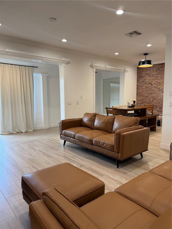 A living room features a brown leather sofa and ottoman with light wood-look flooring — 1413 PORTOFINO MEADOWS BOULEVARD, ORLANDO, FL