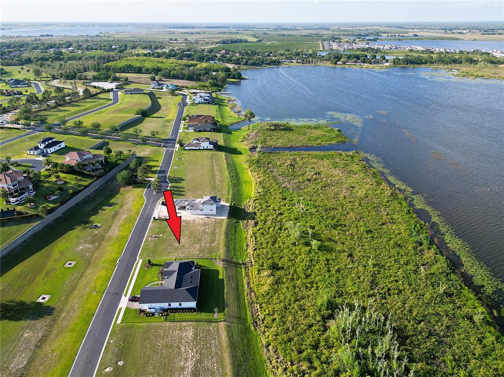 An aerial view shows a residential street with houses bordering a large lake — 328 CALADIUM AVENUE, LAKE ALFRED, FL