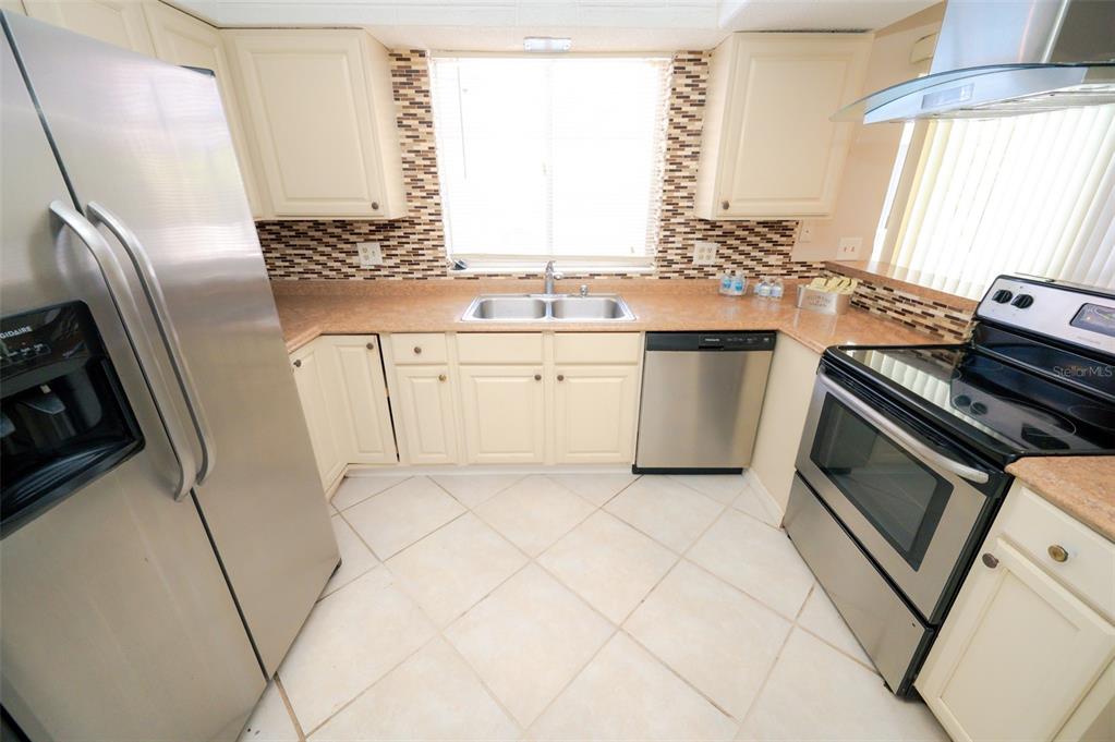 A kitchen with cream cabinets, stainless steel appliances, a double sink, and tiled flooring — 1306 GOLFVIEW DRIVE, DAYTONA BEACH, FL