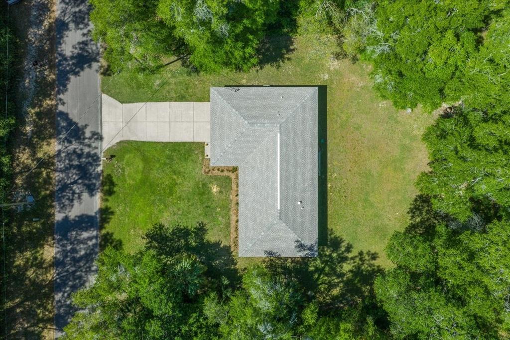 An aerial view shows a house with a gray roof, concrete driveway, and surrounding trees — 3597 E JONAH PLACE, INVERNESS, FL