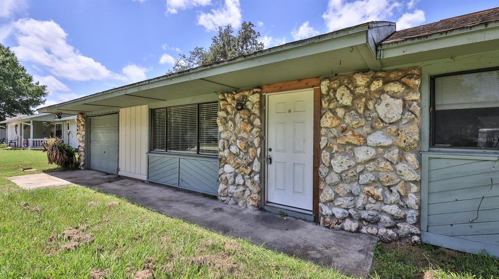 The exterior of a single-story house features a stone facade, a white door, and siding — 2508 PINE TREE DRIVE, EDGEWATER, FL